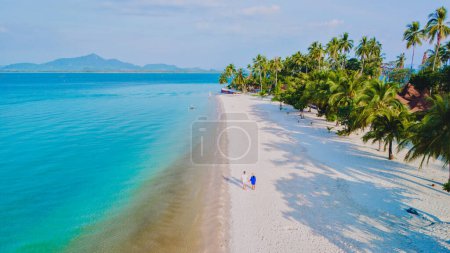 Top view at a couple walking on the white sandy tropical beach of Koh Muk, with palm trees soft white sand, and a turqouse colored ocean in Koh Mook Trang Thailand, man and woman walking on a beach