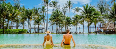 Foto de Un hombre y una mujer están descansando en una piscina con palmeras a su alrededor, disfrutando del agua y el hermoso cielo de arriba. Se están relajando en un paraíso tropical - Imagen libre de derechos