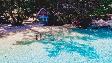 Foto de Vista superior a una pareja en una playa tropical con palmeras y una cabaña de bambú bungalow de madera. Koh Wai Island Trat Tailandia. vista del dron en el hombre joven y la mujer en la playa - Imagen libre de derechos