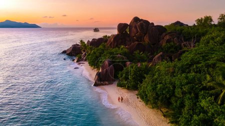 Téléchargez les photos : Drone vue aérienne supérieure de La Digue Seychelles, un couple d'hommes et de femmes marchant sur la plage pendant le coucher du soleil lors de vacances de luxe. Anse Source d'Argent plage La Digue Island Seychelles - en image libre de droit