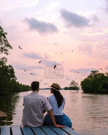 Foto de Águilas marinas al atardecer en el manglar de Chantaburi en Tailandia, águila marina con respaldo rojo, pareja de hombres y mujeres observando la puesta de sol en un muelle de madera, momentos románticos durante un viaje de verano - Imagen libre de derechos