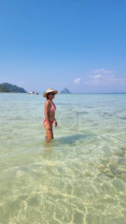 Photo for A graceful woman in a straw hat stands in the ocean, feeling the water embracing her feet as she connects with the sea in a serene moment. Koh Kradan Thailand - Royalty Free Image