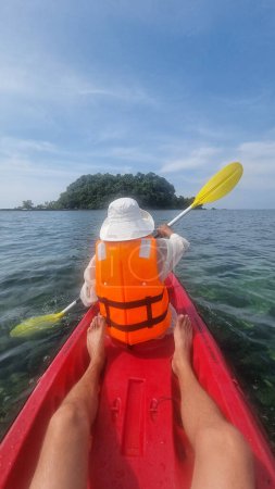 Téléchargez les photos : Une personne dans un kayak rouge vibrant pagaie gracieusement vers une petite île enchanteresse au loin, entourée d'eaux calmes. Koh Libong Thaïlande - en image libre de droit