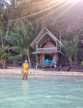 Téléchargez les photos : Une femme en bikini jaune se tient gracieusement dans l'eau, la lumière du soleil reflétant les douces vagues autour d'elle. Koh Wai Thaïlande - en image libre de droit