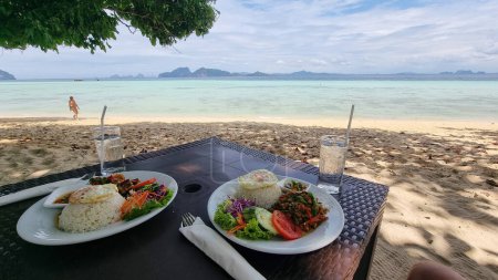 Foto de Una tentadora extensión de platos recién preparados, servidos en platos elegantes sobre una mesa de madera rústica en un vibrante entorno de playa oceánica, comida tailandesa, Koh Kradan Tailandia - Imagen libre de derechos
