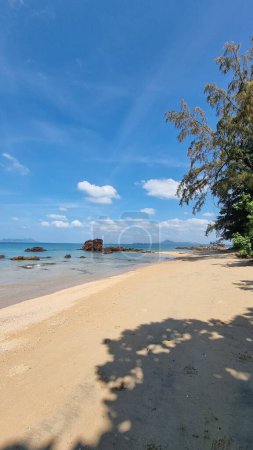 Téléchargez les photos : Une plage de sable tranquille rencontre le vaste océan sous un ciel bleu clair, créant un cadre pittoresque où les vagues embrassent doucement le rivage.Koh Libong Thaïlande - en image libre de droit
