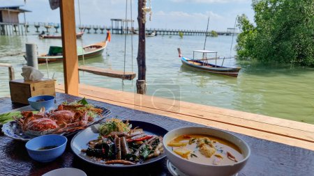 A well-set table adorned with various dishes, surrounded by the serene waters of a lake or ocean, creating a picturesque setting for a delicious meal. Koh Libong Thailand 