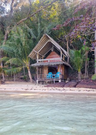 A quaint hut nestled on a sandy beach, adorned with a table and chairs inviting relaxation by the sea.