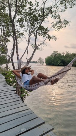 Photo for A woman relaxes in a hammock on a dock, enjoying the peaceful waters and gentle breeze on a sunny day. Chantaburi Thailand - Royalty Free Image