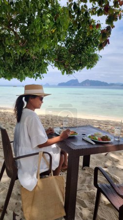 Une femme s'assoit paisiblement à une table sur la plage de sable, profitant de la vue tranquille sur l'océan et du bruit des vagues qui s'écrasent. Koh Kradan Thaïlande