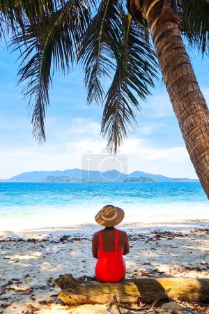 Téléchargez les photos : Une silhouette solitaire se trouve sous un majestueux palmier sur une plage de sable, à la recherche de réconfort et de tranquillité dans un cadre serein. Koh Wai Thaïlande - en image libre de droit