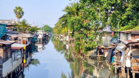 Téléchargez les photos : Bangkok Thaïlande 13 janvier 2024, Une rivière serpente à travers un charmant village, flanqué de maisons de chaque côté, créant une scène pittoresque de vie urbaine tranquille en harmonie avec la nature. - en image libre de droit