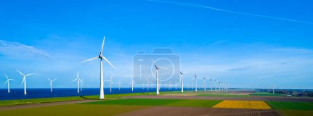 Photo for A picturesque scene of windmills gracefully spinning in a row on a lush green field beside the vast ocean, under the Spring sun. windmill turbines - Royalty Free Image