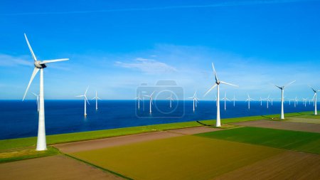 Foto de Una impresionante escena se desarrolla mientras un grupo de molinos de viento se alzan en un campo junto al océano en los Países Bajos Flevoland durante la vibrante temporada de primavera. día de la tierra, ecológico, energía verde - Imagen libre de derechos