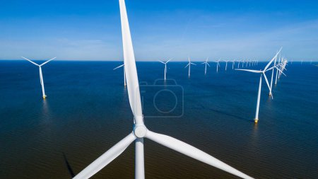Eine Ansammlung von Windrädern, die die Kraft der Meeresbrise im niederländischen Flevoland an einem lebhaften Frühlingstag anmutig nutzen. Drohne Luftaufnahme von Windkraftanlagen grüne Energie im Meer