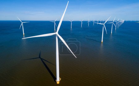 Foto de Un grupo de molinos de viento elegantes flotan con gracia sobre la superficie tranquila y reflectante del agua en Flevoland durante la vibrante temporada de primavera. vista aérea de drones de turbinas de molino de viento energía verde - Imagen libre de derechos