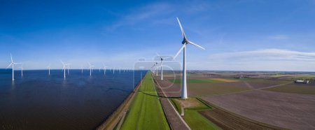 Photo for A stunning view of a row of wind turbines gracefully turning along the horizon of a vast body of water in Flevoland, Netherlands during the vibrant season of Spring. - Royalty Free Image