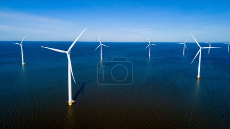 Eine Gruppe von Windrädern dreht sich an einem ruhigen Frühlingstag elegant im Meer vor der Küste der Niederlande in Flevoland. Drohnen-Luftaufnahme von Windkraftanlagen grüne Energie im Meer