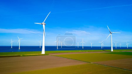Foto de Un grupo de molinos de viento se encuentra alto en un campo al lado del océano, sus cuchillas girando con gracia en la brisa primaveral. aerogeneradores, energía verde, día de la tierra - Imagen libre de derechos