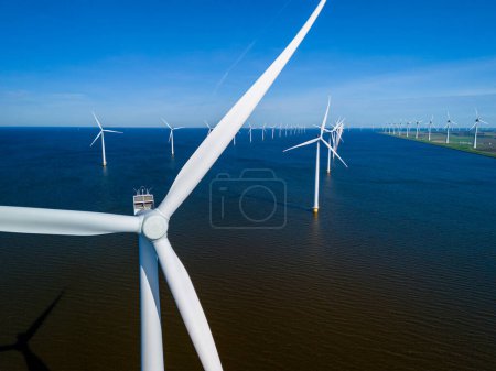 Photo for A group of picturesque windmills from the Netherlands Flevoland region gracefully float atop a tranquil body of water on a beautiful Spring day. windmill turbines green energy in the ocean - Royalty Free Image