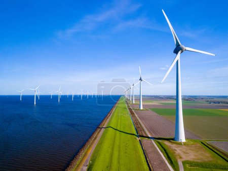 Foto de Una hilera de elegantes turbinas eólicas se alzan junto a un vasto cuerpo de agua en los Países Bajos Flevoland, reflejando la armonía entre la naturaleza y las energías renovables. - Imagen libre de derechos