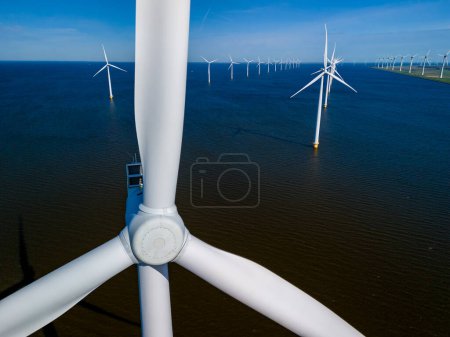 Foto de Parque eólico sereno en el océano frente a la costa de Flevoland, Países Bajos, con filas de majestuosas turbinas de molino de viento que capturan con gracia la brisa primaveral. turbinas de molinos de viento energía verde en el océano - Imagen libre de derechos
