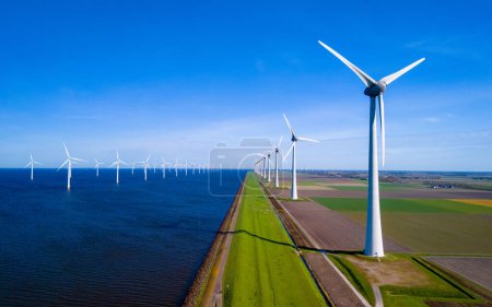 Eine beeindruckende Reihe von Windkraftanlagen in der wunderschönen Landschaft des niederländischen Flevoland während der frischen Frühjahrssaison. grüne Energie, Energiewende, Windkraftanlagen an Land und in den Ozeanen