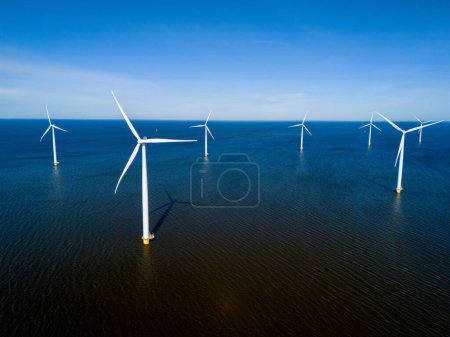 Foto de Un grupo de aerogeneradores se mantiene alto en el océano, aprovechando el poder del viento para generar energía renovable en los Países Bajos Flevoland durante la vibrante temporada de primavera. - Imagen libre de derechos