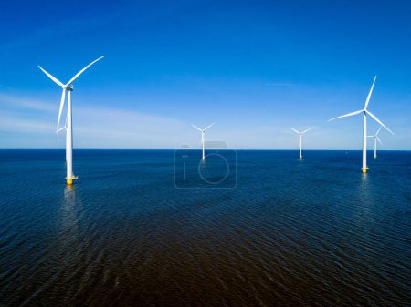 Eine Gruppe von Windrädern dreht sich während der pulsierenden Frühlingszeit anmutig über der Meeresoberfläche im niederländischen Flevoland. Drohne Luftaufnahme von Windkraftanlagen grüne Energie 