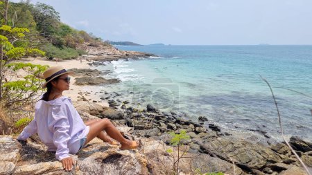 Koh Samet Island Thailand, thailändische Asiatinnen sitzen auf einem Felsen und blicken über die Bucht mit einem tropischen Strand und einem blauen Ozean