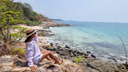 Koh Samet Island Thailand, thailändische Asiatinnen mit Hut sitzen auf einem Felsen und blicken auf die Bucht mit tropischem Strand und blauem Ozean