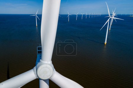 Foto de Los rayos de sol iluminan un vasto parque eólico en el océano, mostrando filas de elegantes turbinas de molino de viento de pie en los Países Bajos Flevoland durante la vibrante temporada de primavera. - Imagen libre de derechos