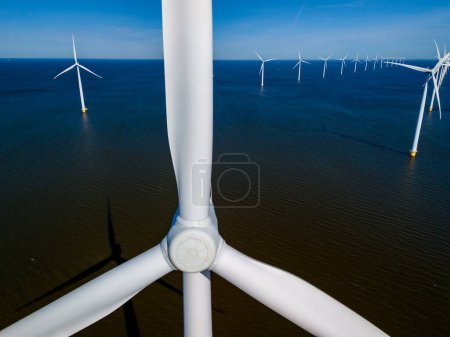 An aerial view of a wind farm featuring rows of windmill turbines gracefully rotating in the vast expanse of the ocean, captured in the Netherlands Flevoland during the vibrant season of Spring.