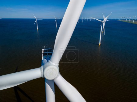 Foto de Una vista impresionante se despliega mientras las turbinas de molino de viento cosechan con gracia la energía del viento en medio de un vasto cuerpo de agua en la región holandesa de Flevoland durante la vibrante temporada de primavera. - Imagen libre de derechos