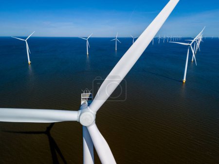 Majestic windmill turbines rise from the waters of the Netherlands Flevoland, spinning gracefully in the spring breeze. drone aerial view of windmill turbines green energy in the ocean