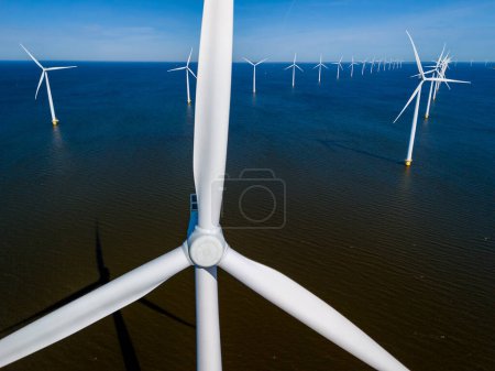 Foto de Un grupo de imponentes turbinas eólicas se encuentra alto en el océano, sus cuchillas girando graciosamente en la brisa primaveral, aprovechando el poder del viento para producir energía limpia. - Imagen libre de derechos