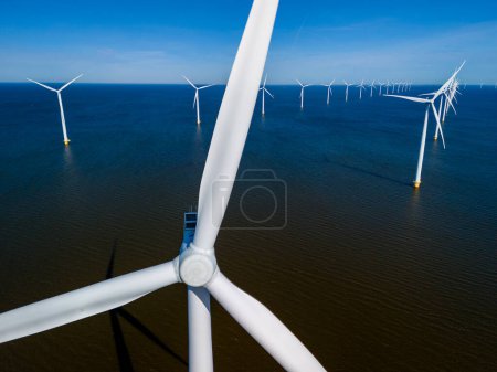A group of majestic wind turbines stand tall in the ocean off the coast of the Netherlands Flevoland, harnessing the power of the wind to generate clean energy. drone aerial view of windmill turbines