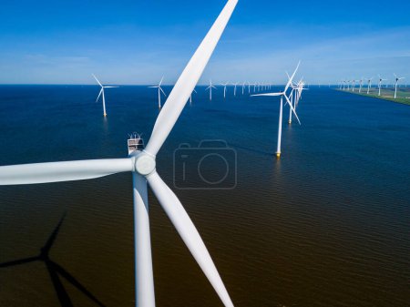 A large group of windmills stands tall in the tranquil waters of Flevoland, creating a harmonious and sustainable energy landscape in the springtime. windmill turbines in ocean