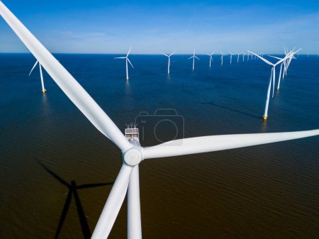 Foto de Un parque eólico en medio del océano en los Países Bajos Flevoland, con turbinas de molinos de viento girando graciosamente bajo el cielo primaveral. vista aérea de drones de turbinas de molino de viento energía verde en el océano - Imagen libre de derechos