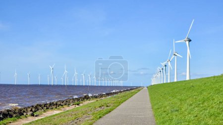 Foto de Parque de molinos de viento en alta mar y un cielo azul, parque de molinos de viento en el océano. Países Bajos Europa. turbinas de molino de viento en el Noordoostpolder Flevoland, carretera en un dique holandés - Imagen libre de derechos