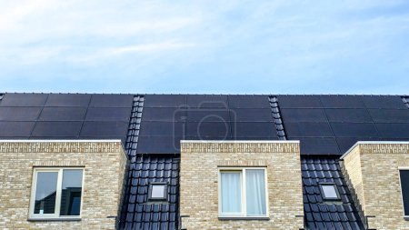 Foto de Casa familiar holandesa con paneles solares negros en el techo contra un cielo soleado Primer plano de un edificio nuevo con paneles solares negros. Zonnepanelen, Zonne energie, Traducción: Panel solar, Energía solar - Imagen libre de derechos