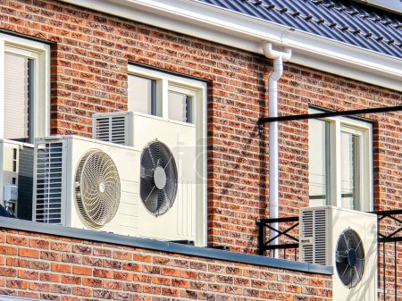 Foto de Primer plano de una unidad de bomba de calor de fuente de aire instalada al aire libre en una casa moderna con paneles solares en los Países Bajos. Zonnepanelen, pompa caliente, Traducción: Panel solar, Bomba de calor - Imagen libre de derechos