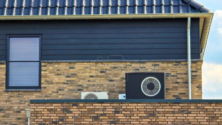 Foto de Unidad de bomba de calor de fuente de aire instalada al aire libre en una casa moderna con ladrillos en los Países Bajos en primavera, bomba de calor de fuente de aire de traducción de pompa caliente, aire acondicionado y bomba de calor de fuente de aire - Imagen libre de derechos
