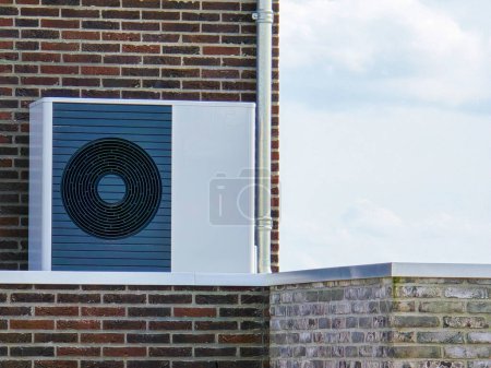 Téléchargez les photos : Unité de pompe à chaleur de source d'air installée à l'extérieur dans une maison moderne avec briques aux Pays-Bas au printemps, pompe à chaleur de source d'air de traduction de pompe à chaleur, transition énergétique du gaz naturel à l'électricité - en image libre de droit