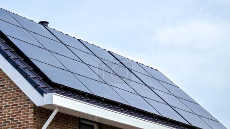 Foto de Casas de nueva construcción con paneles solares negros en el techo contra un cielo soleado, zona suburbana holandesa. Zonnepanelen, Zonne energie, Traducción: Panel solar, Energía solar - Imagen libre de derechos