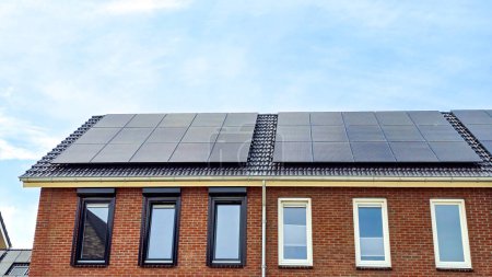 Téléchargez les photos : Maisons nouvellement construites avec des panneaux solaires noirs sur le toit contre un ciel ensoleillé Gros plan du nouveau bâtiment avec des panneaux solaires noirs. - en image libre de droit