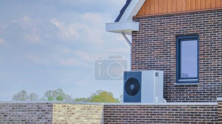 Téléchargez les photos : Unité de pompe à chaleur de source d'air installée à l'extérieur dans une maison moderne avec briques aux Pays-Bas au printemps, pompe à chaleur de source d'air de traduction de pompe à chaleur, transition énergétique en Europe - en image libre de droit