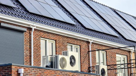 Foto de Unidad de bomba de calor de fuente de aire instalada al aire libre en una casa moderna con paneles solares en los Países Bajos, nueva casa con paneles solares negros. Zonnepanelen, Zonne energie, Traducción: Panel solar, Energía solar - Imagen libre de derechos