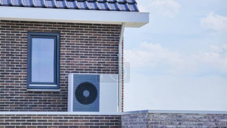 Foto de Unidad de bomba de calor de la fuente de aire instalada al aire libre en una casa moderna con ladrillos en los Países Bajos en primavera, bomba de calor de la fuente de aire de la traducción de la pompa caliente, residuos cero respetuosos del medio ambiente - Imagen libre de derechos