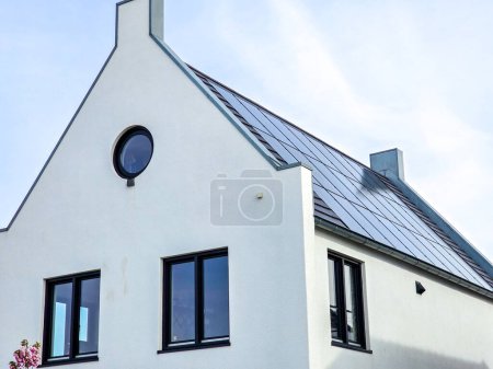Téléchargez les photos : Maisons nouvellement construites avec des panneaux solaires noirs sur le toit contre un ciel ensoleillé Gros plan du nouveau bâtiment avec des panneaux solaires noirs. Zone de banlieue néerlandaise avec des maisons familiales modernes - en image libre de droit